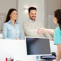 A man and woman shaking hands with the dental receptionist upon their arrival