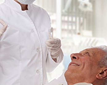 Older man in dental chair smiling at dentist