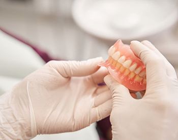 Gloved hands holding upper and lower dentures