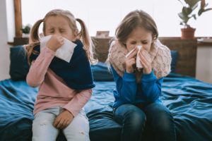 two little girls sitting on a bed and blowing their noses 